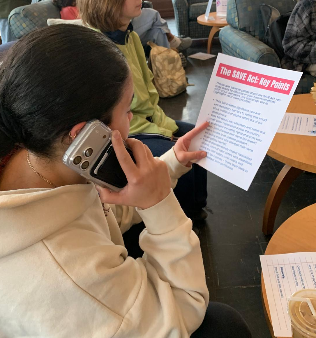 A student on a phone call reading a Camels Vote SAVE Act flyer at a phone-banking session.