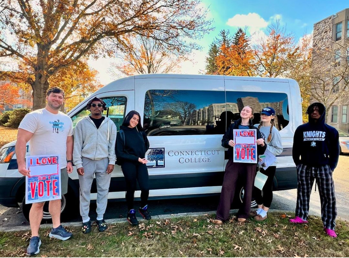Students holding “I LOVE VOTING” signs in front of a Connecticut College van that shuttled voters to the polls.