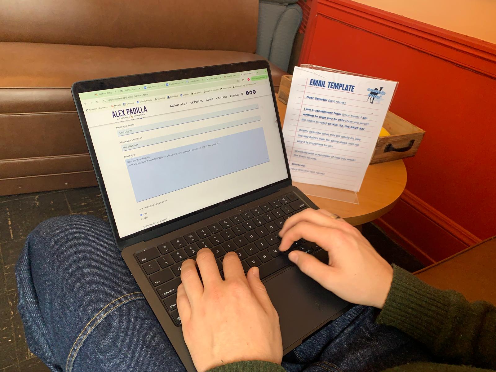 A student types an email to Senator Alex Padilla using the Camels Vote email template card on the table beside their laptop.