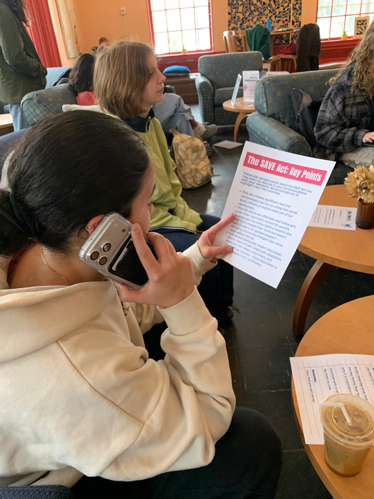 A student on the phone with a senator’s office, reading from a “SAVE Act: Key Points” handout.